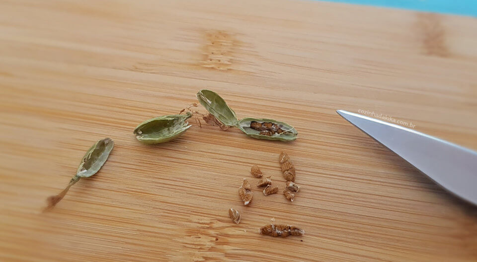 Bagas de cardamomo abertas com as sementes espalhadas sobre uma tábua de madeira