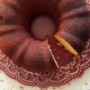 Bolo de fubá, em um prato vermelho decorado, sobre uma toalha em tons pasteis estampada de flores