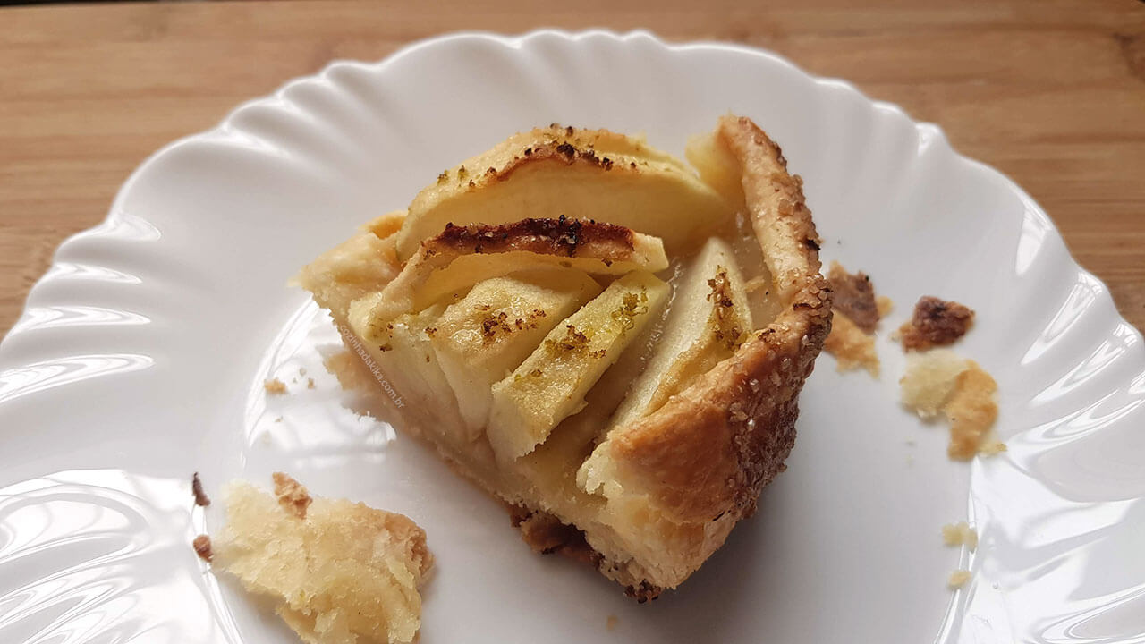 Fatia de torta de maçã num prato branco, sobre uma tábua de madeira