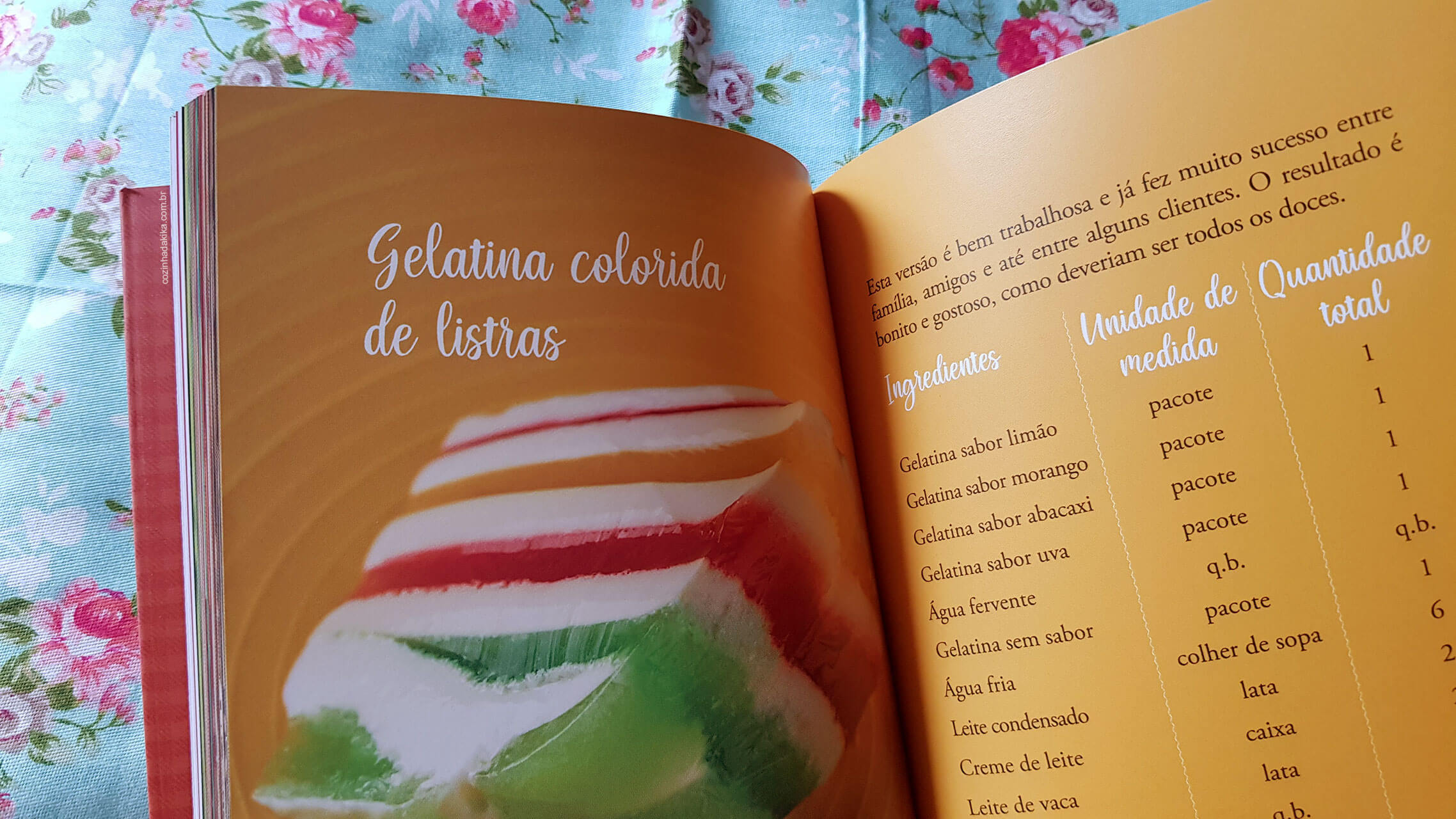 Livro Doçuras de Domingo sobre um tecido florido. O livro está aberto numa página que mostra a receita de uma gelatina colorida em camadas.